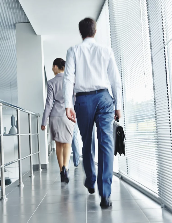 a woman in a dress nad a man in a white shirt and blue pants carrying a briefcase are walking down a hallway